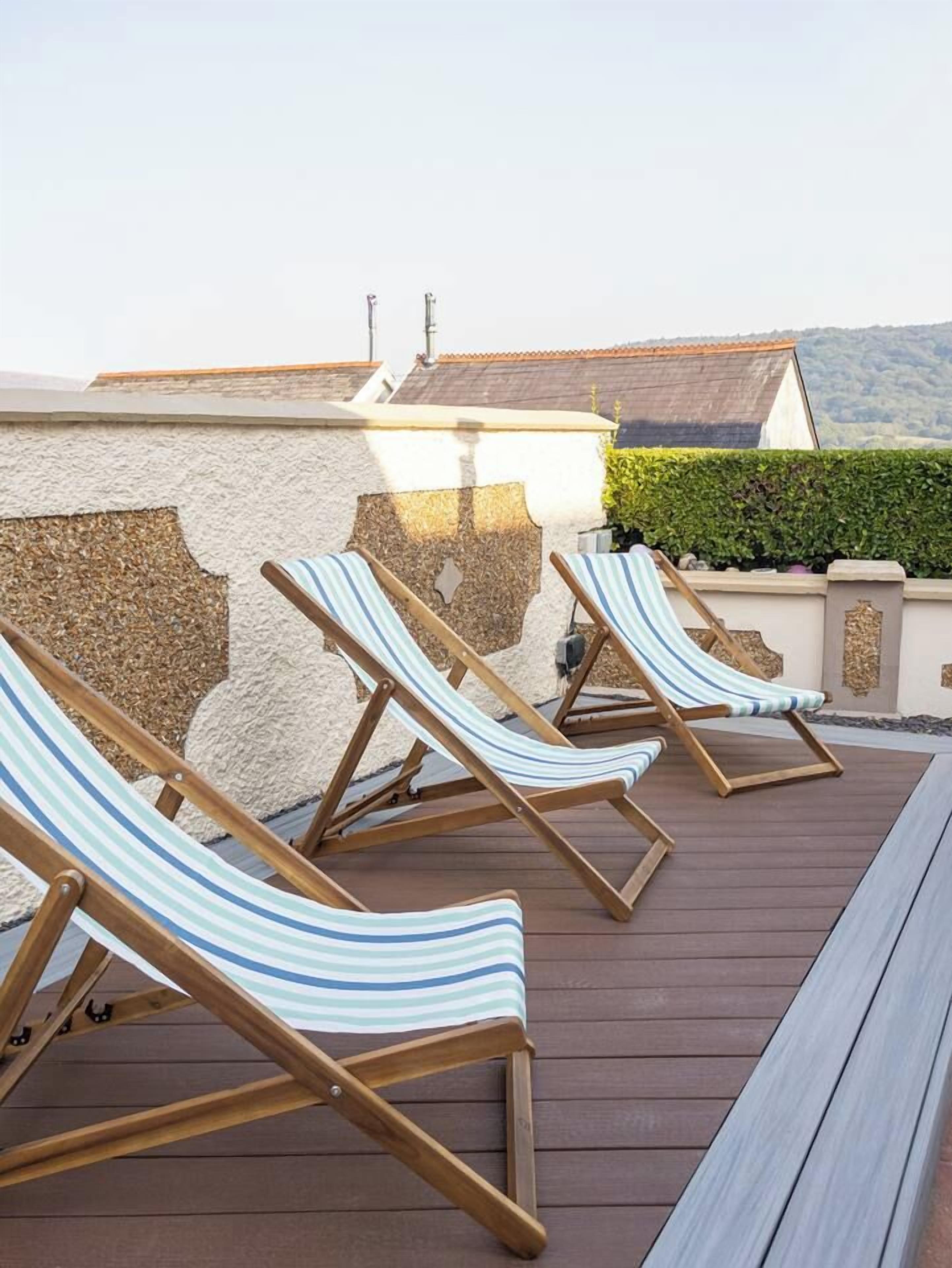 Eine Terrasse mit drei gestreiften Liegestühlen und einer Holzbank.