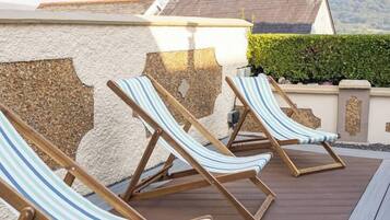 Eine Terrasse mit drei gestreiften Liegestühlen und einer Holzbank.