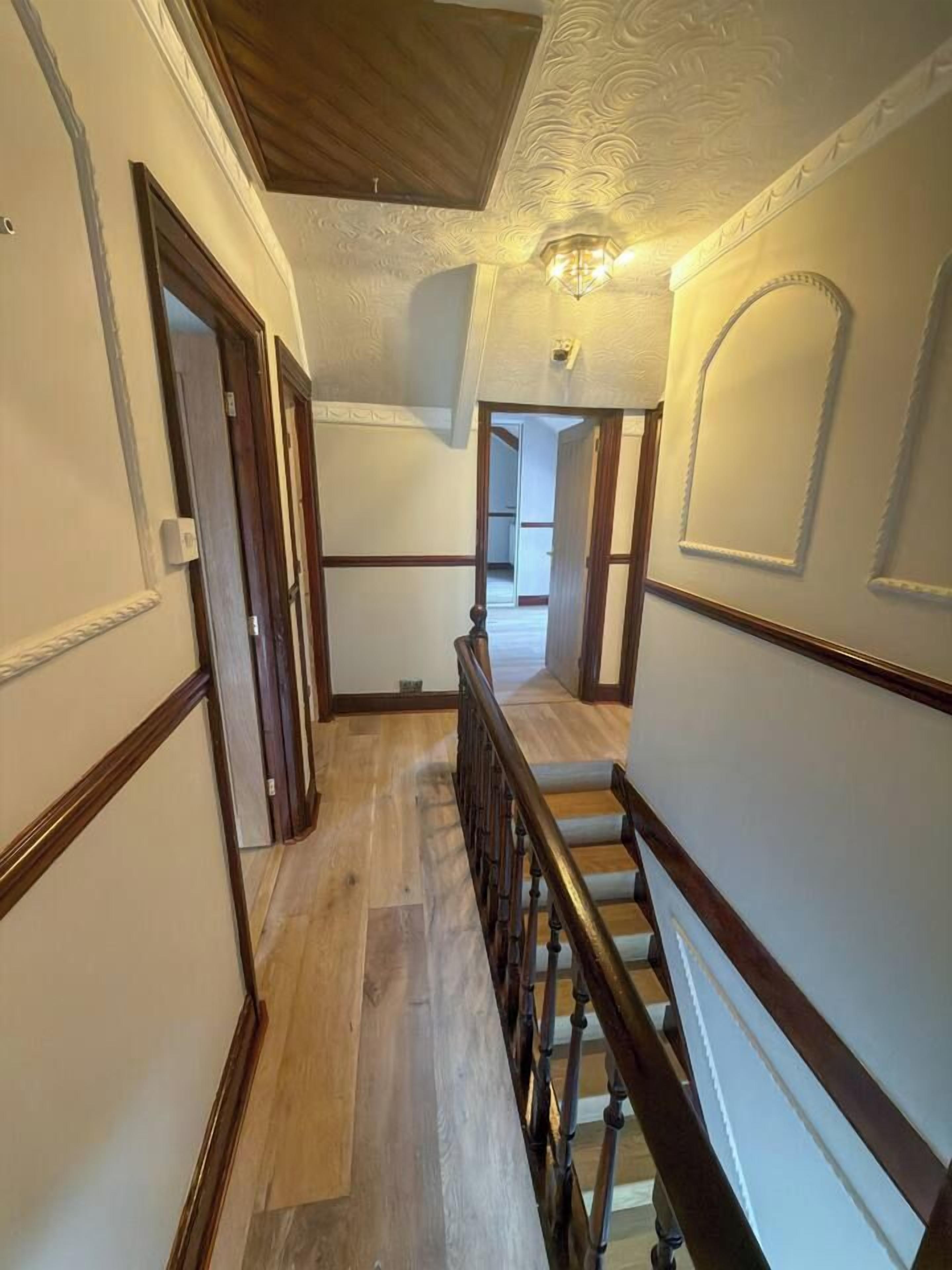 A hallway with wooden flooring, a wooden railing, and a ceiling with decorative molding.