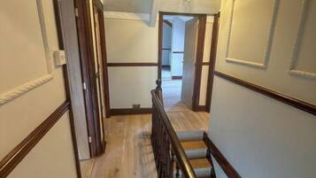 A hallway with wooden flooring, a wooden railing, and a ceiling with decorative molding.