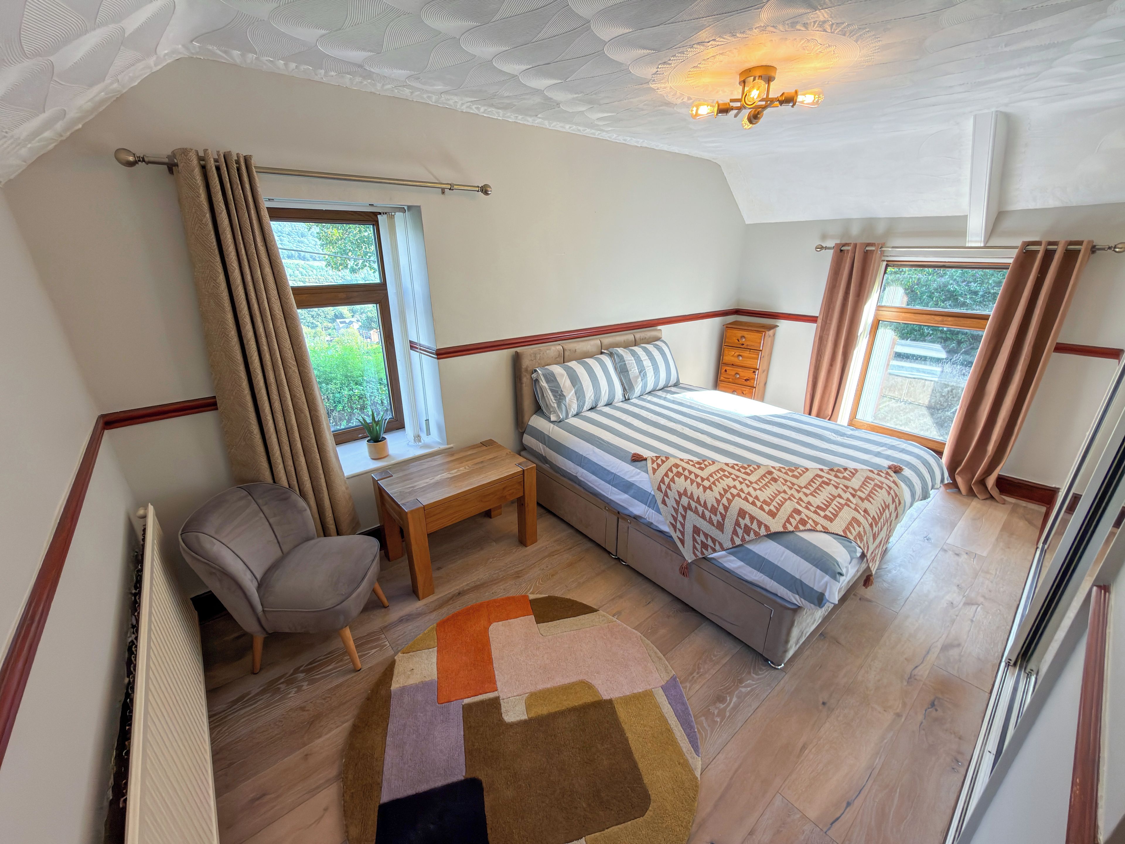 Ein Schlafzimmer mit Bett, Nachttisch, Stuhl, Fenster und Deckenleuchte.