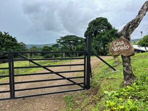Une entrée fermée par un portail, sur laquelle on peut lire l’inscription « Casa Venado », située dans un cadre rural, avec des arbres et un ciel dégagé.