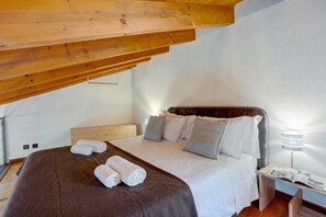 Une chambre avec un plafond en bois, un lit avec une literie blanche et une table de chevet avec une lampe.