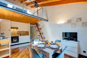 Une cuisine moderne avec des meubles blancs, un coin repas doté d’une table en bois et un téléviseur posé sur un meuble.