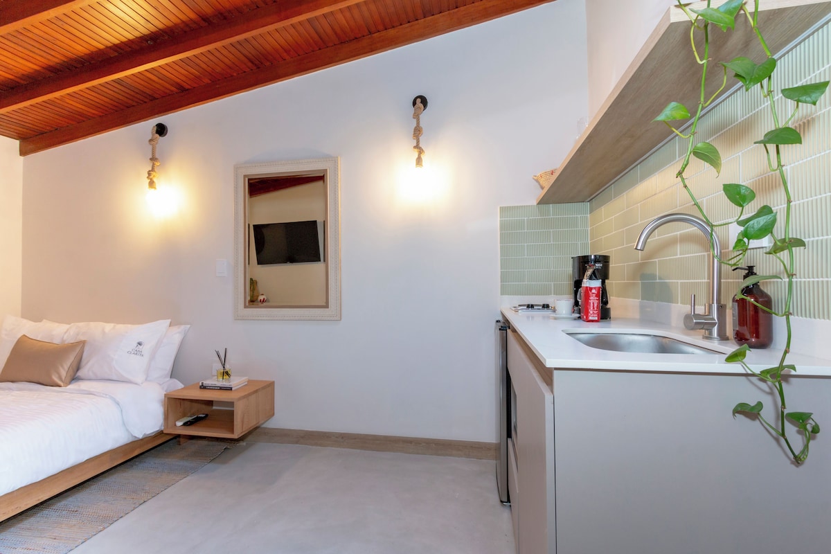 Un dormitorio moderno con techo de madera, una mesita de noche con control remoto y una cama con ropa de cama blanca.