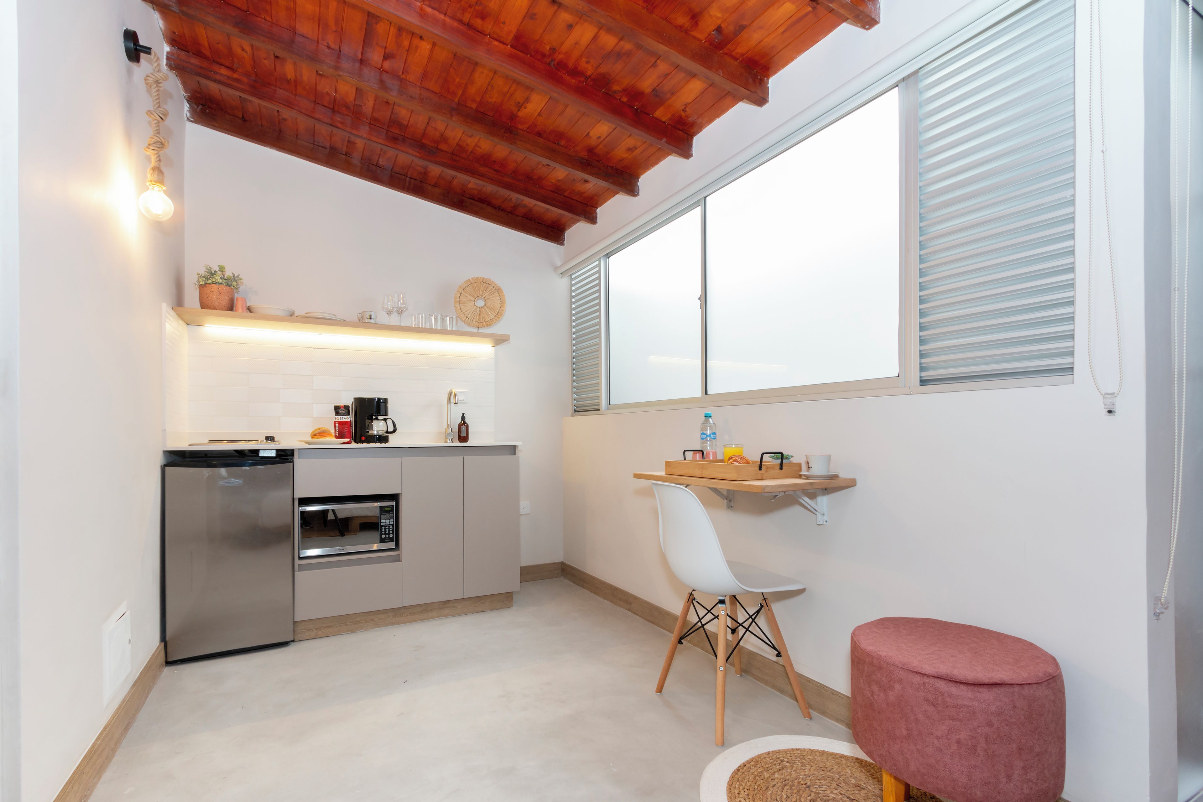 Cocina compacta con horno integrado, cafetera y pequeño comedor con una silla y una mesa.