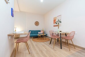 Una sala de estar moderna con un sofá, una mesa de comedor con sillas, una alfombra pequeña y una obra de arte colgada en la pared.
