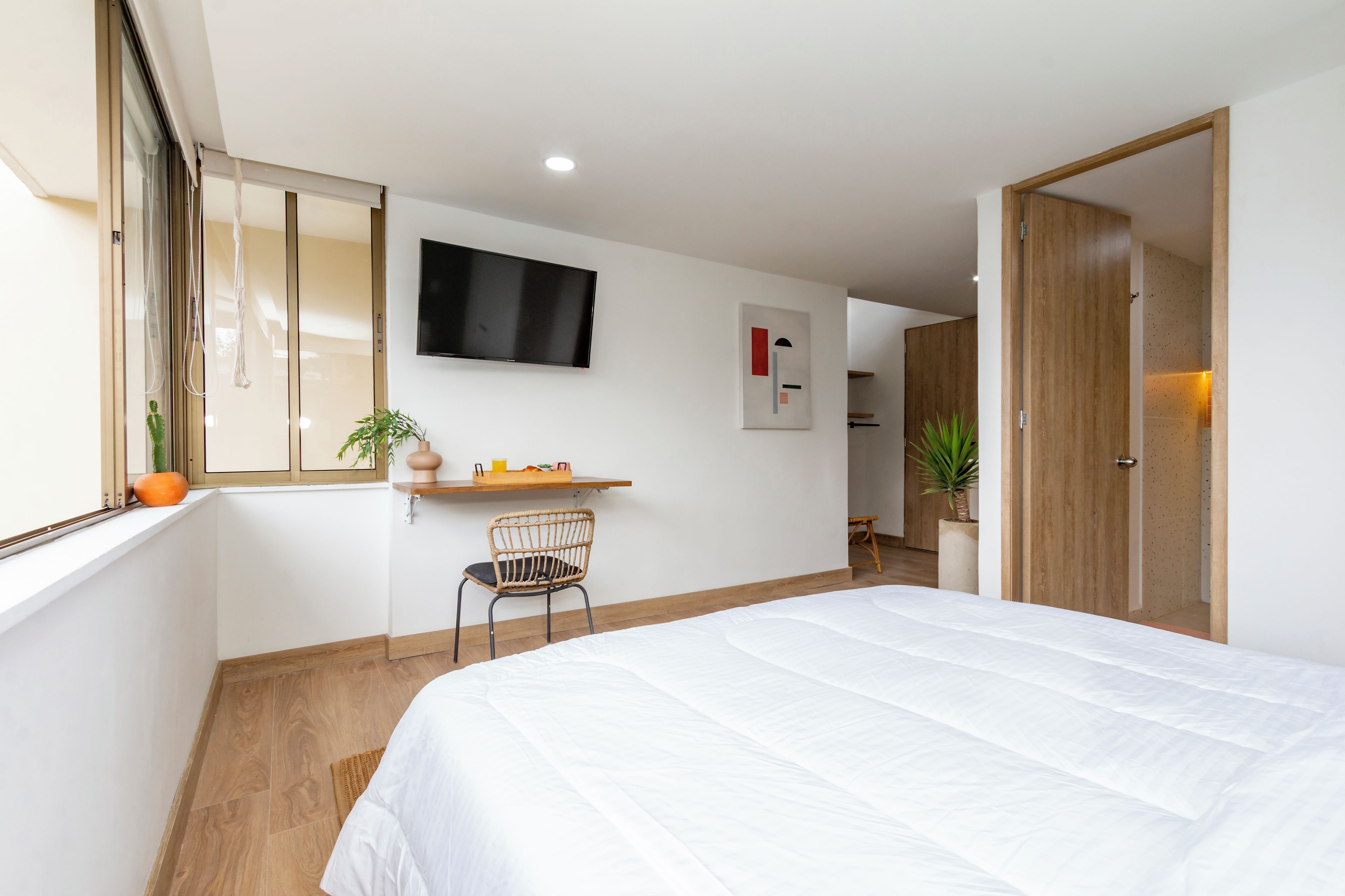 A hotel room with a bed, a desk, a chair, a TV, and a door.