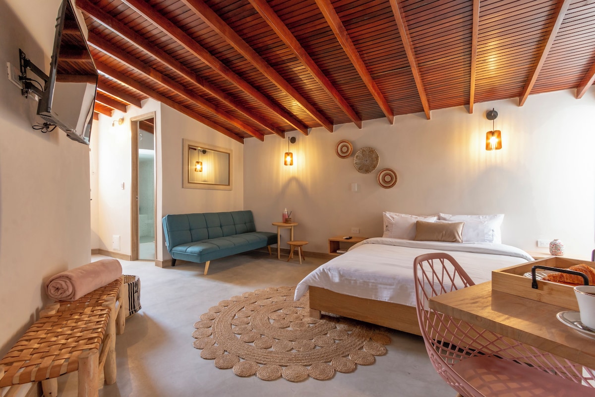 Un dormitorio con una cama, un sofá azul, una silla de madera, una mesita y una alfombra tejida.