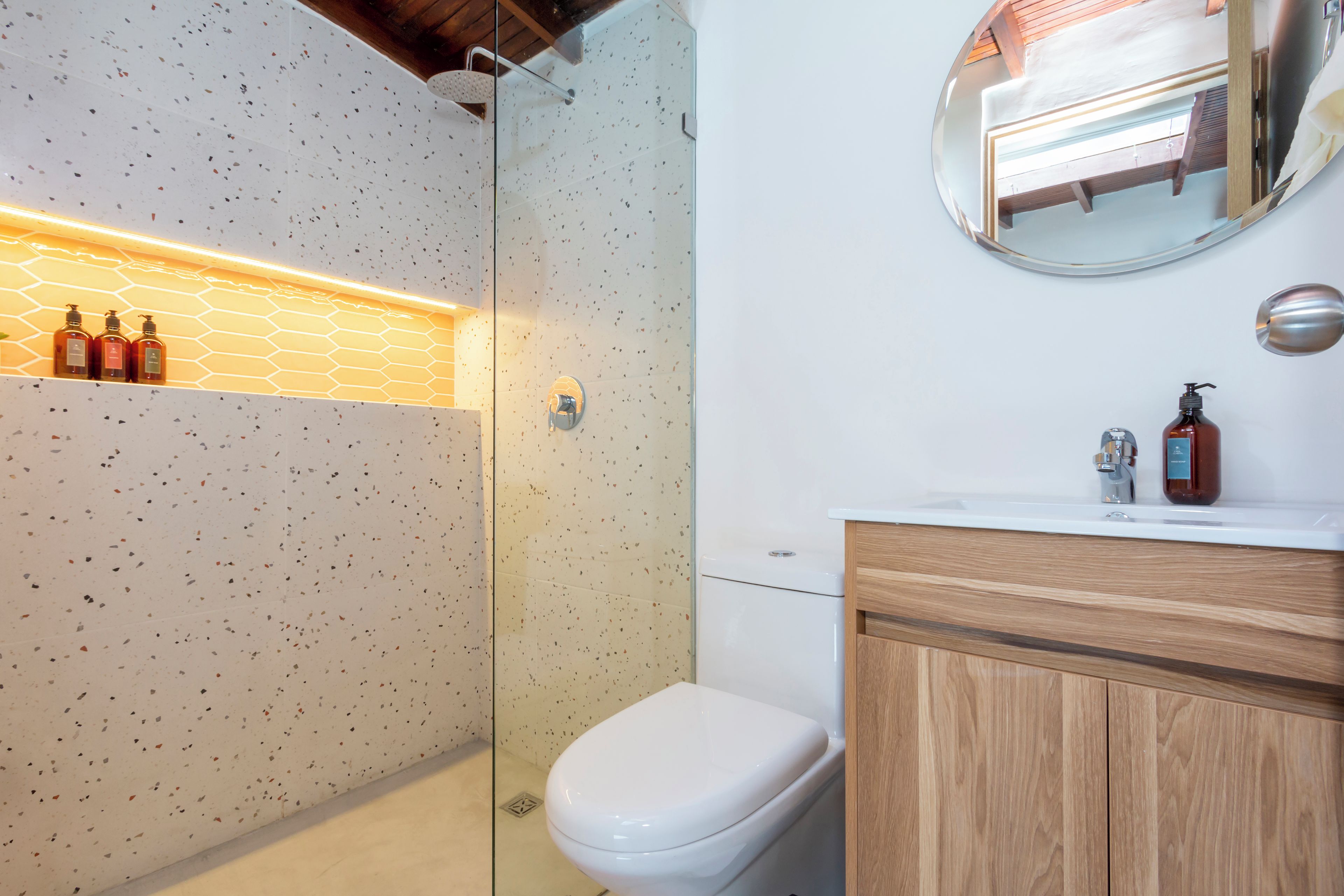 A modern bathroom with a glass shower enclosure, a white toilet, a wooden vanity, and a mirror above the sink.