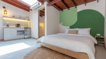 A bedroom with a bed, a green accent wall, a kitchen area with a microwave, and a wooden ceiling.