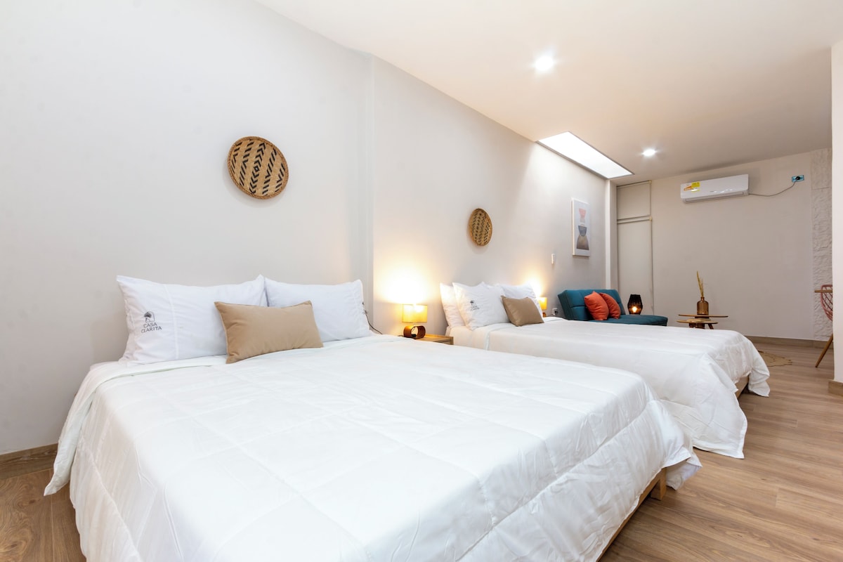 Habitación de hotel con dos camas, un sofá, una lámpara y un equipo de aire acondicionado.