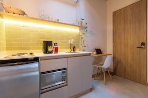 Cocina compacta con microondas integrado, cafetera y pequeño comedor con una silla.
