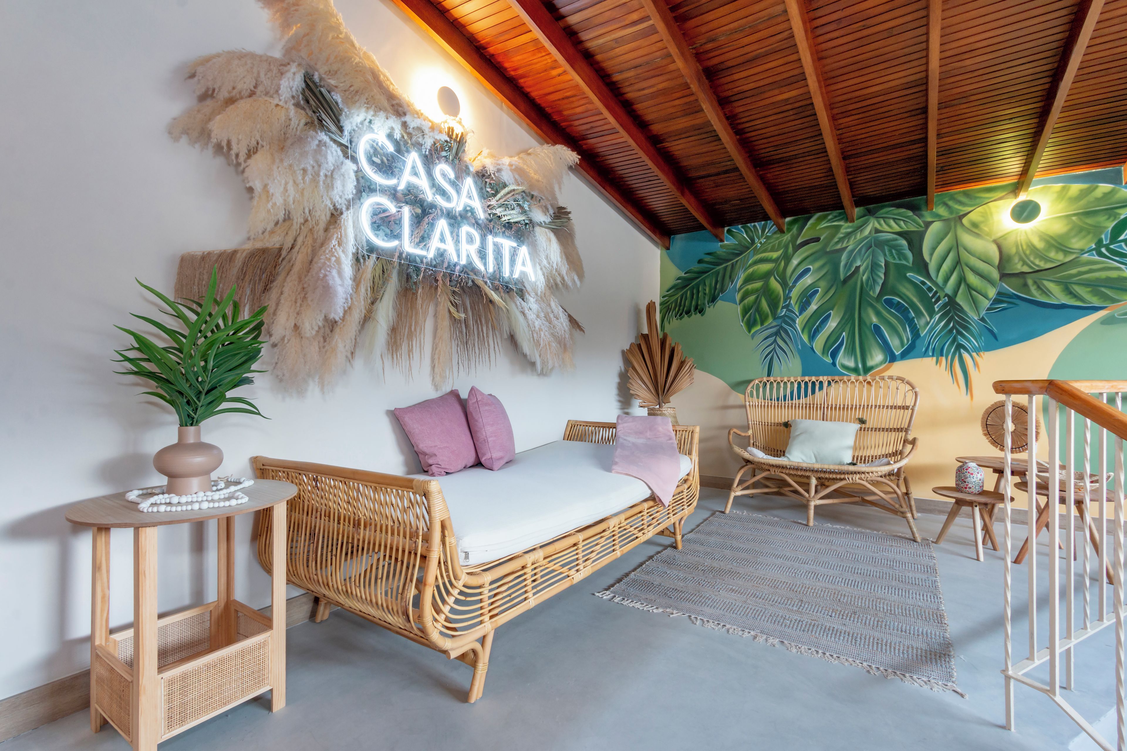 Una habitación acogedora con un sofá de ratán, una mesita con una planta y un letrero en la pared que dice 'CASA CLARITA'.
