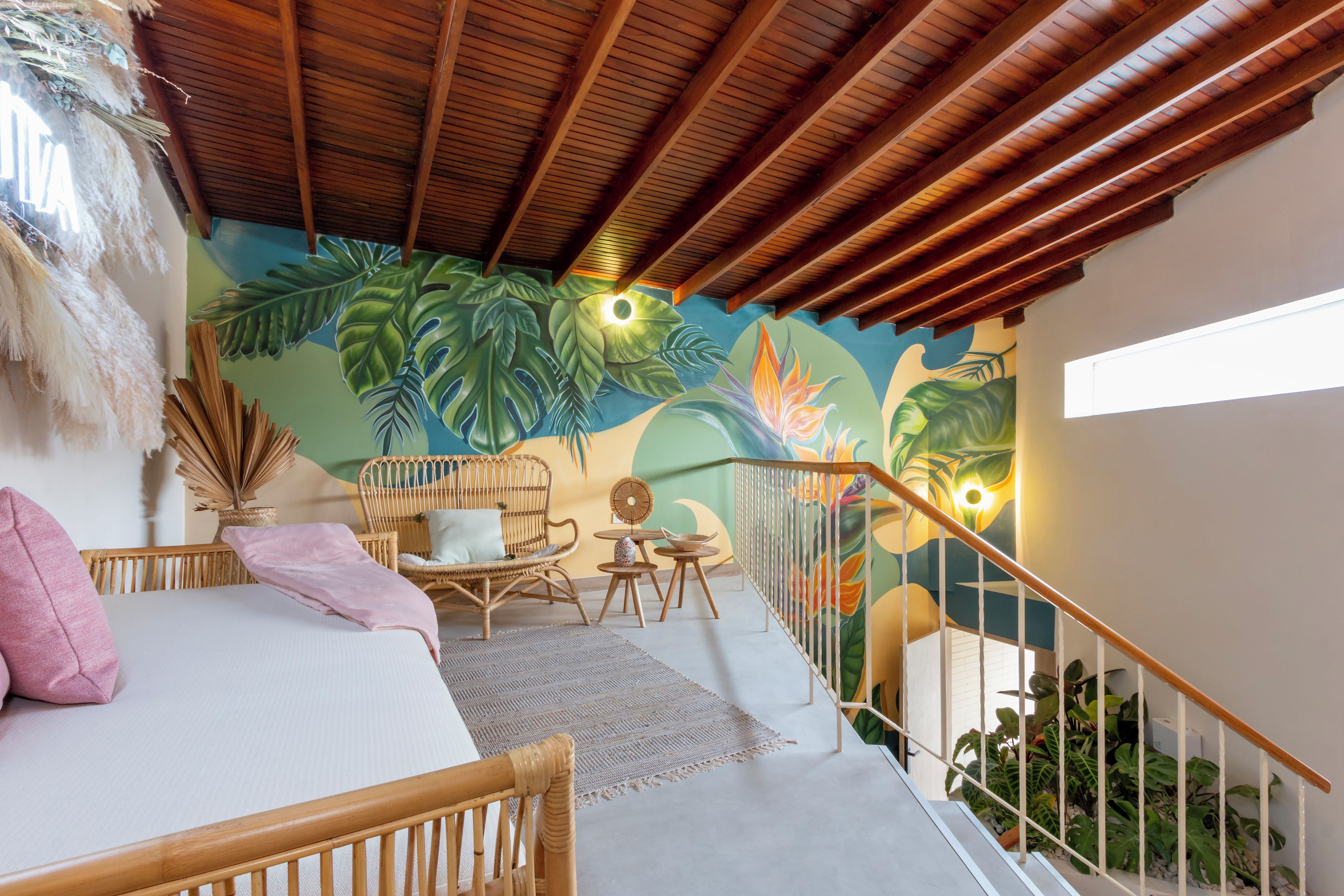 Una habitación con una cama, una silla de mimbre, una mesita pequeña y una escalera con barandilla.