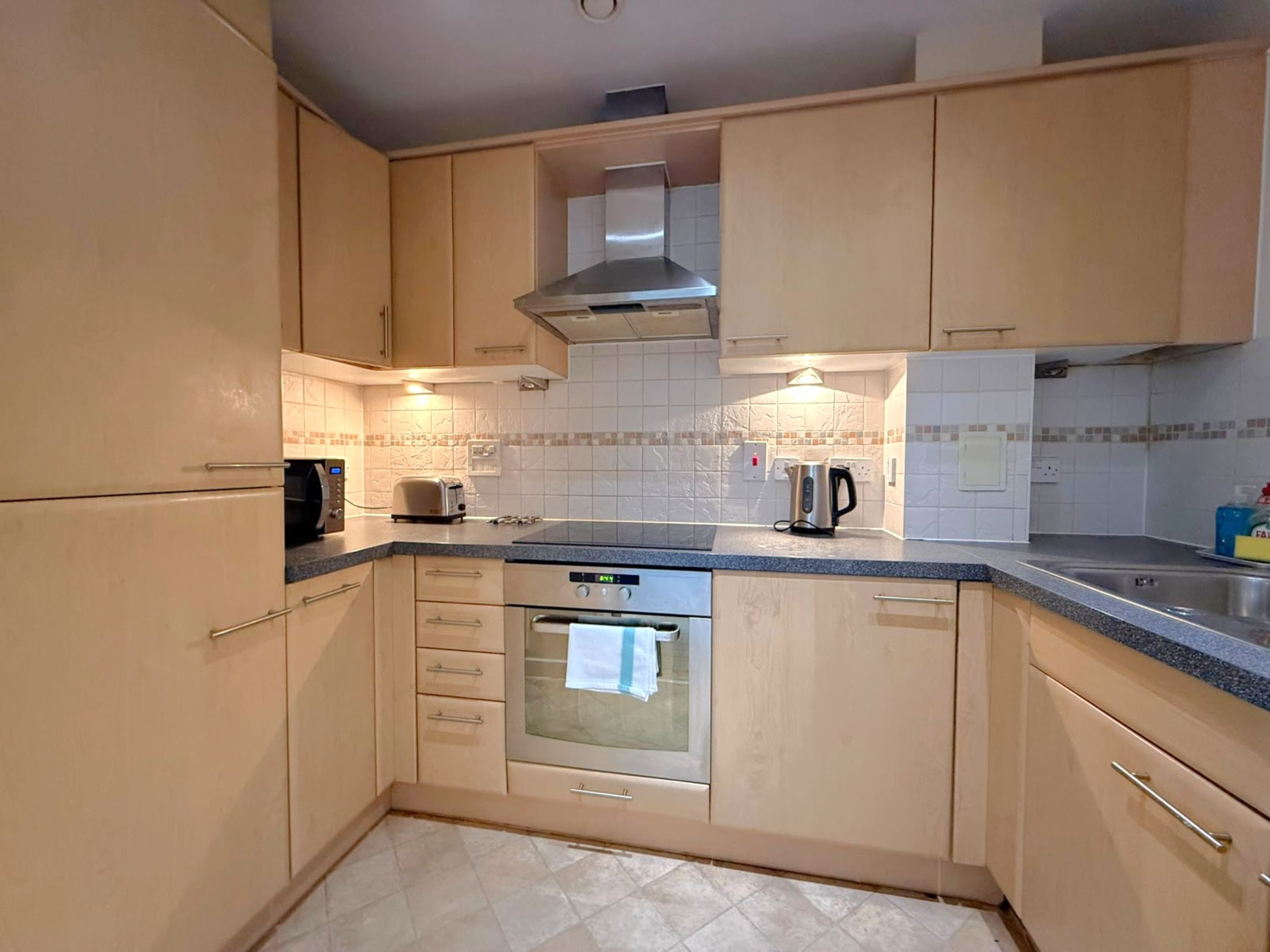 A compact kitchen with wooden cabinets, a built-in oven, a microwave, and a kettle.