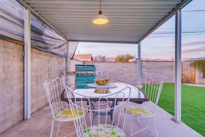 A covered patio with a table and chairs, a grill, and a view of a mountain range. - Atomic Agave, Mid-Century Tucson Retreat (Tucson)