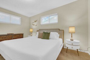 A bedroom with a large bed, two bedside tables with lamps, a dresser, and two windows with blinds. - Atomic Agave, Mid-Century Tucson Retreat (Tucson)