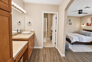 Ein Hotelzimmer mit einem Holznähtisch, einem Bett, einem Deckenventilator und einem Badezimmer mit Dusche und Toilette.