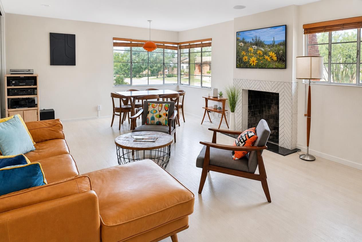A living room with a leather sofa, a dining table with chairs, a fireplace, and large windows.