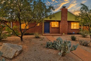 A brick house with a blue door, surrounded by desert vegetation and a clear sky. - Cactus Comeback, A Retro Tucson Retreat (Tucson)