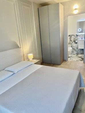 Ein Hotelzimmer mit Bett, Nachttischlampe, Kleiderschrank und einem durch eine geöffnete Tür einsehbaren Badezimmer.