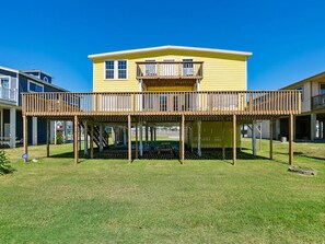 A two-story yellow house with a wooden deck and a balcony. - Passing Winds (Galveston)