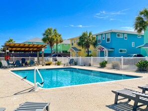 A swimming pool with lounge chairs and a covered seating area, surrounded by colorful buildings. - Port A's Casita Azul (Port Aransas)