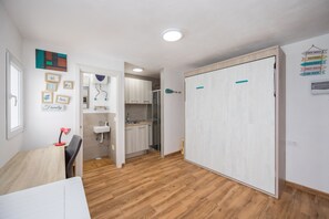 Ein moderner, hell erleuchteter Raum mit Holzboden, einem Schreibtisch mit Stuhl, einem Bett und einem Kleiderschrank.