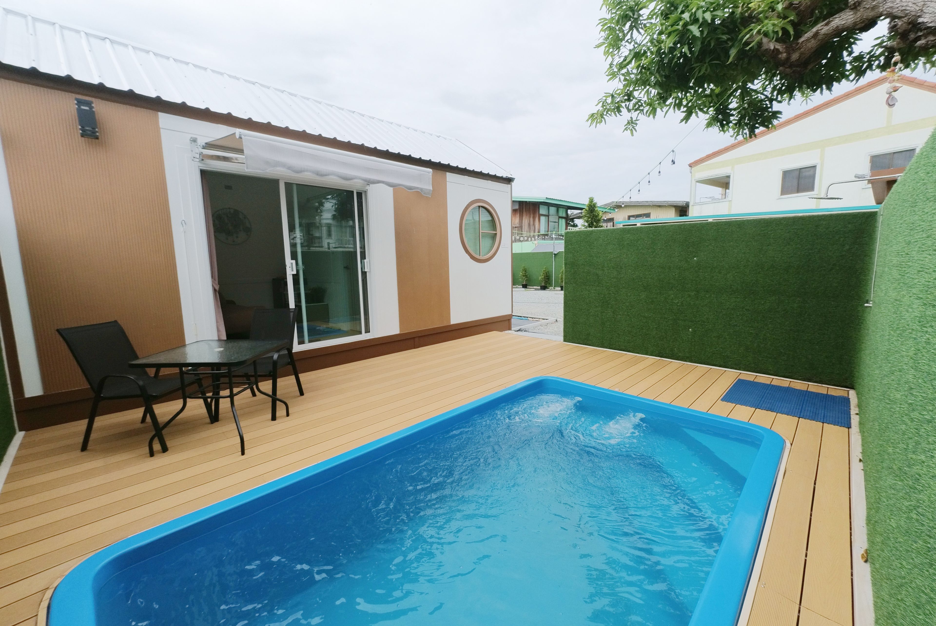 Una piscina con cubierta de madera, una mesa con sillas y un ventanal que da a un espacio interior.