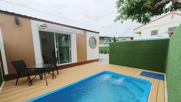 Una piscina con cubierta de madera, una mesa con sillas y un ventanal que da a un espacio interior.