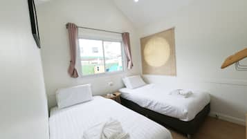 A bedroom with two beds, a window with curtains, a bedside table with a lamp, and a view of the outside.