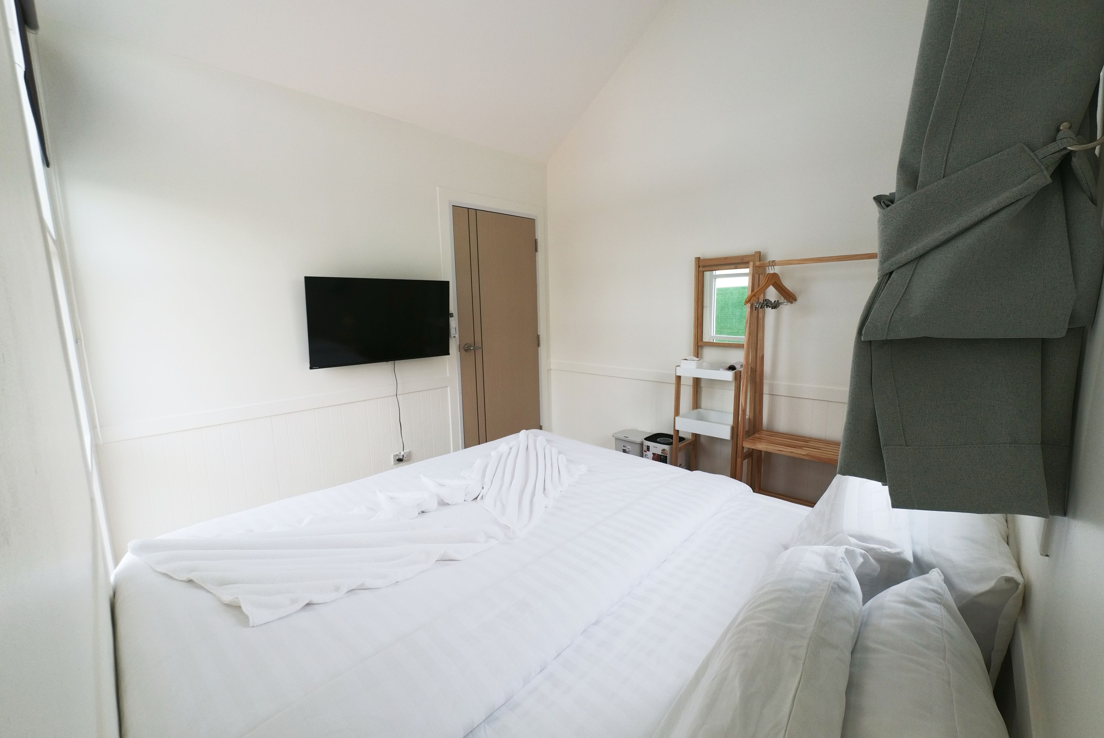 A hotel room with a bed, a television, a wardrobe, a mirror, and a towel rack.