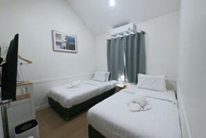 A hotel room with two beds, a desk, a chair, a hanging coat, and a picture on the wall.