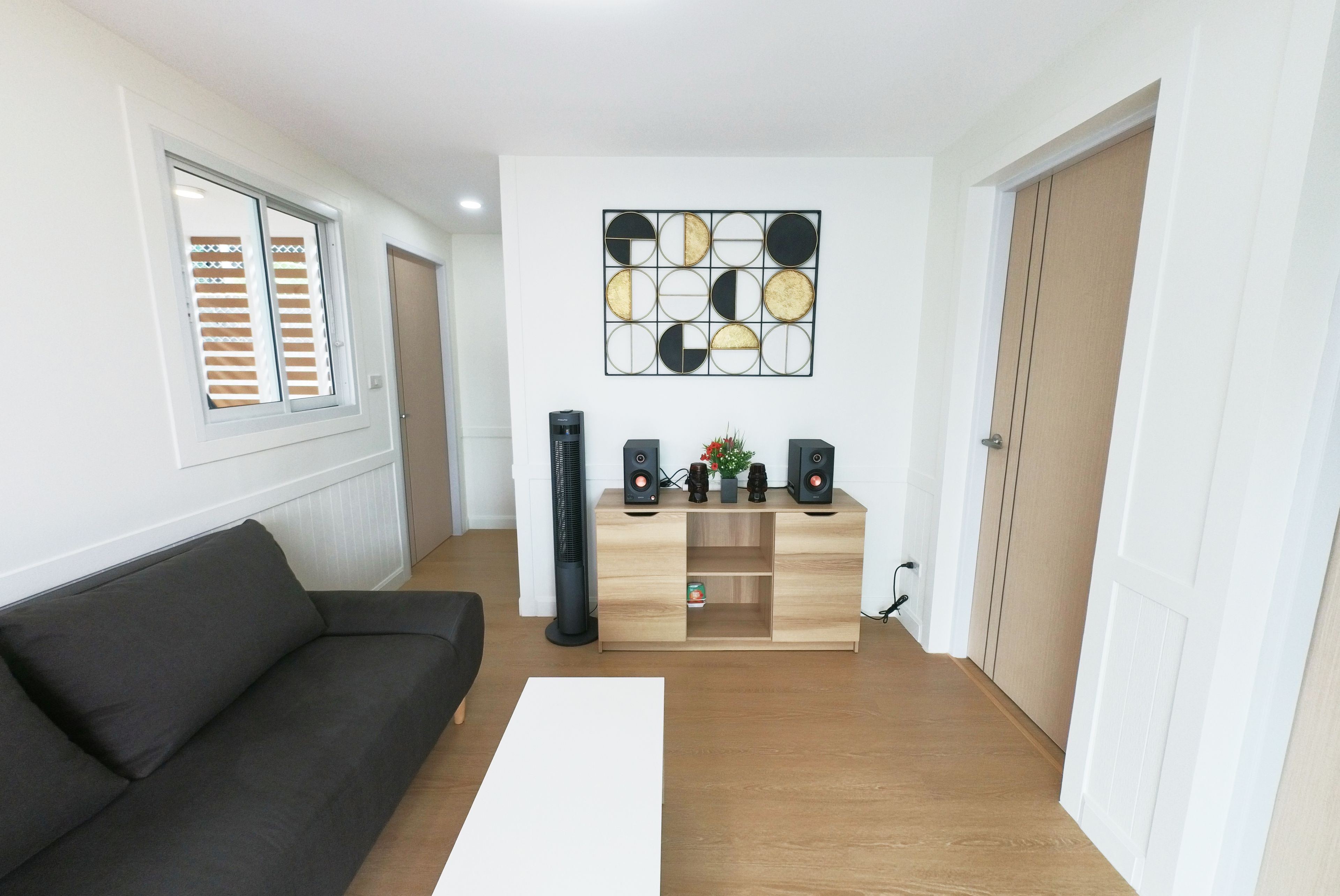 A modern living room with a sofa, a coffee table, a wall-mounted speaker system, and a decorative wall art piece.