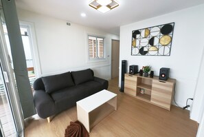 A modern living room with a dark sofa, a white coffee table, a wooden cabinet with speakers, and a wall art piece. - 49 Pool Villa Bangsaen (Mueang Chonburi)