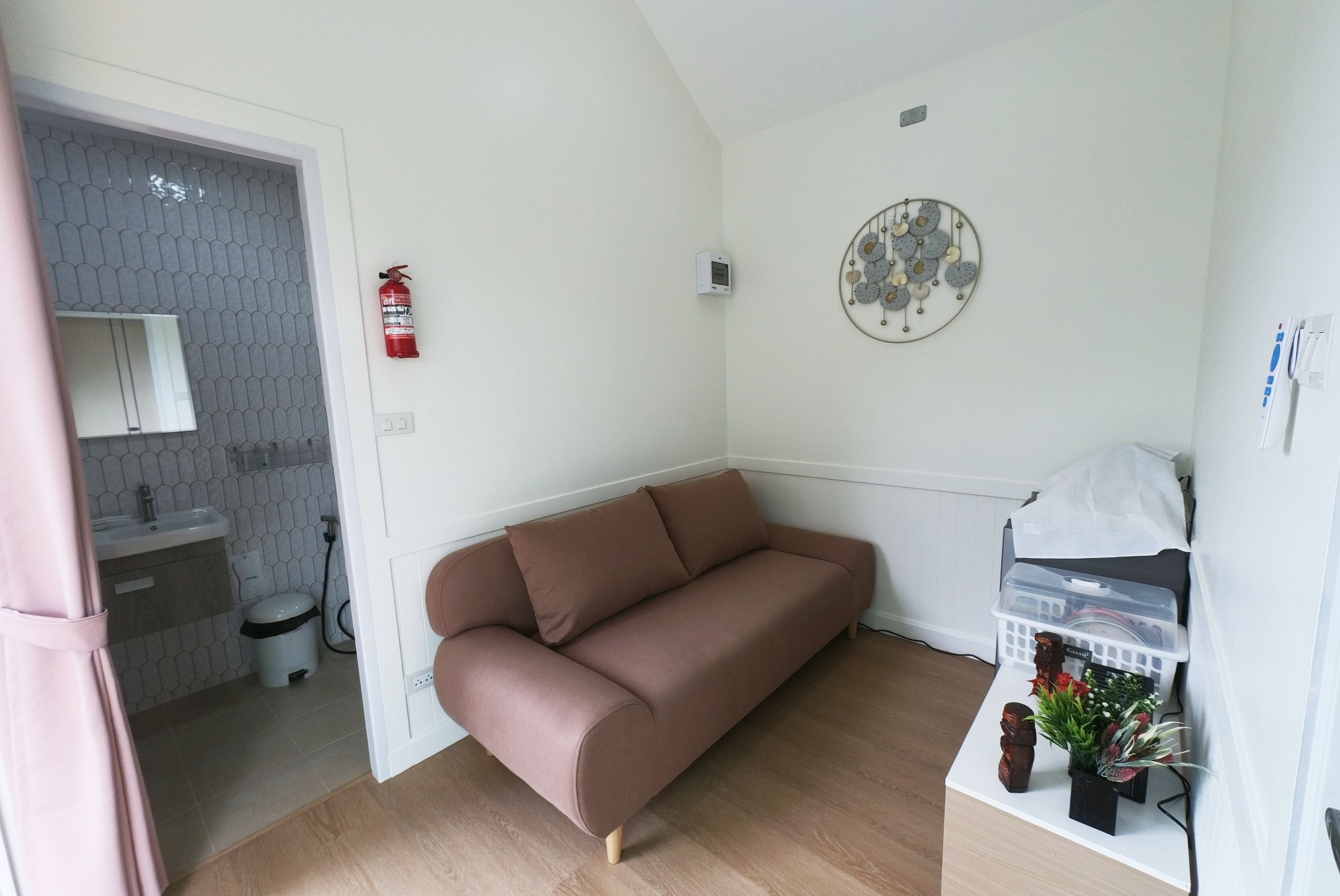 Ein kleiner, moderner Wohnraum mit einer Couch, einem an der Wand befestigten dekorativen Gegenstand, einem Feuerlöscher und einem kleinen Tisch mit einem Korb.