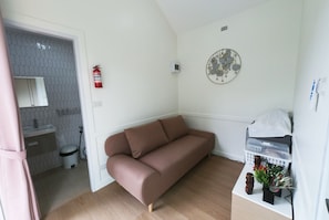 A small, modern living space with a sofa, a wall-mounted decorative item, a fire extinguisher, and a small table with a basket. - 49 Pool Villa Bangsaen (Mueang Chonburi)