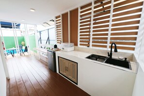 A compact kitchen with a built-in sink, a small refrigerator, and a window with blinds. - 49 Pool Villa Bangsaen (Mueang Chonburi)