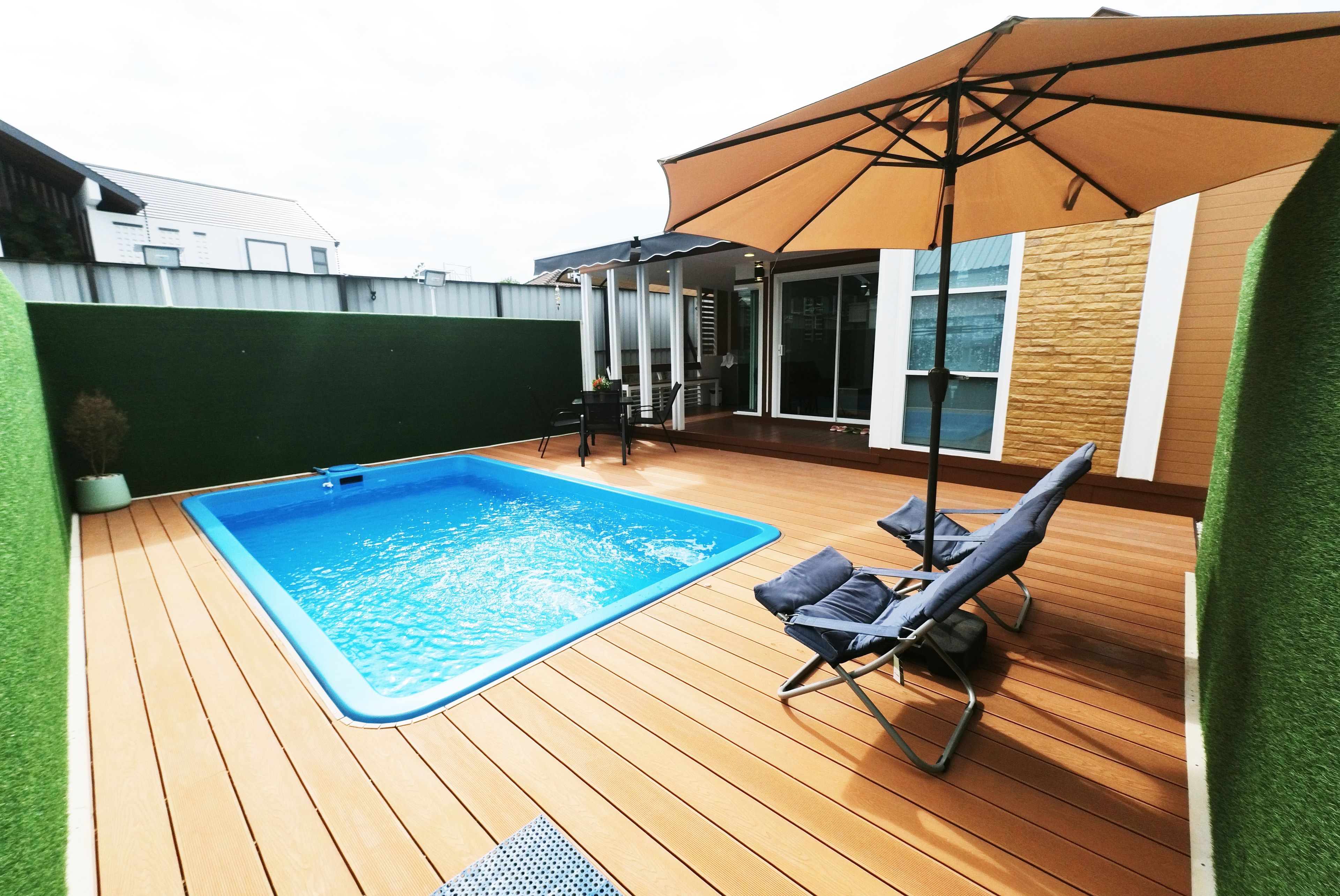 Una piscina con muelle de madera, una silla de descanso y una zona de patio techada.