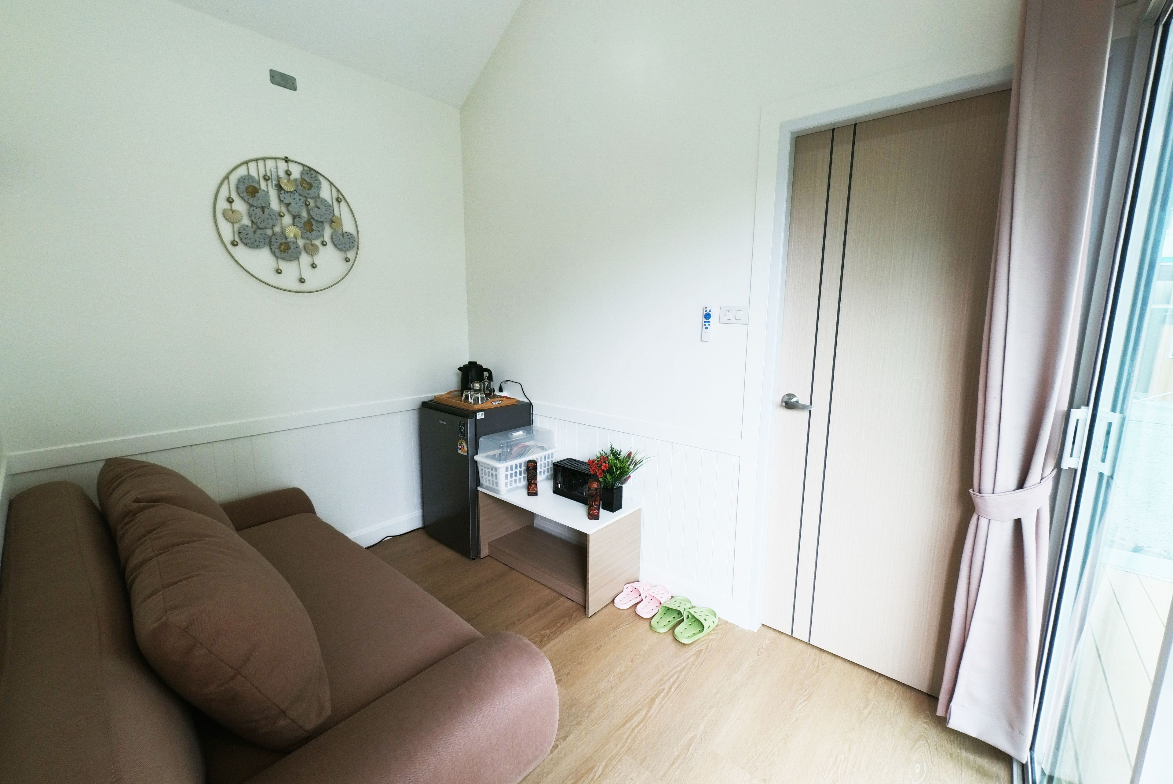 Una sala de estar con un sofá marrón, una mesita con un hervidor, un refrigerador y una puerta con picaporte.