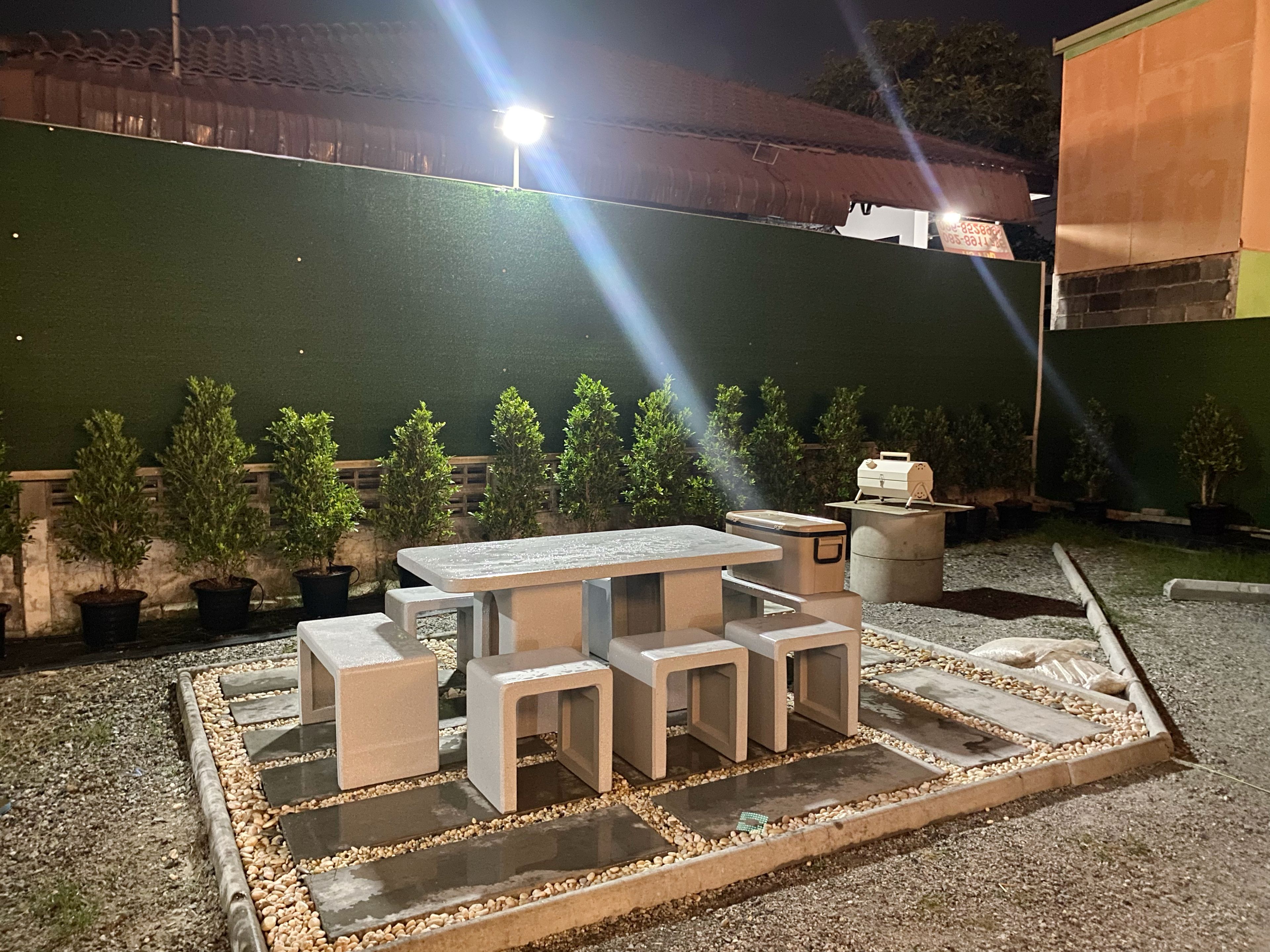 Un área de estar al aire libre con una mesa y bancos, rodeada de plantas en macetas.