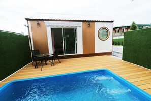 A poolside area with a wooden deck, a small table with chairs, and a glass door leading to an interior space. - 49 Pool Villa Bangsaen (Mueang Chonburi)