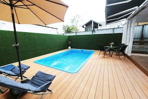 A swimming pool with lounge chairs and a table, surrounded by a wooden deck and a green wall. - 49 Pool Villa Bangsaen (Mueang Chonburi)