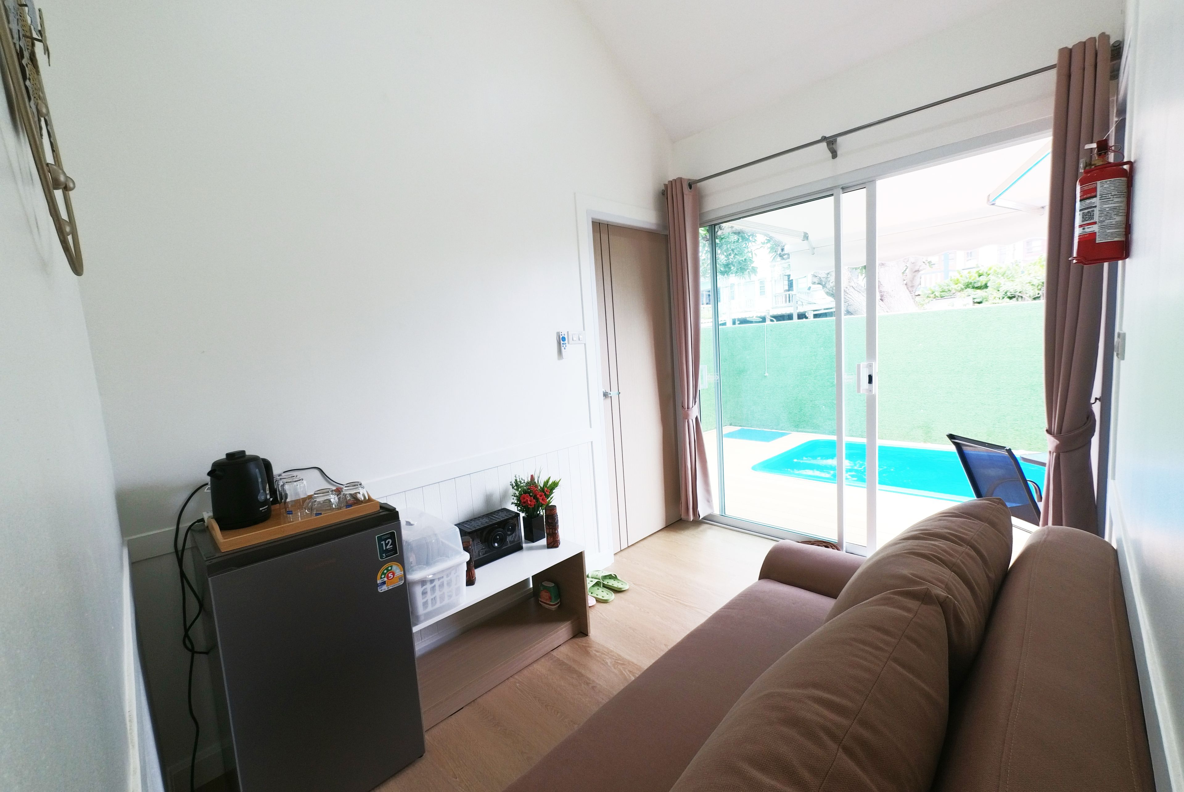 Habitación con sofá, cafetera, radio y vista a una piscina por una puerta corrediza.