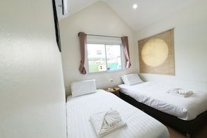 A bedroom with two beds, a window with curtains, a bedside table with a lamp, and a view of the outside.