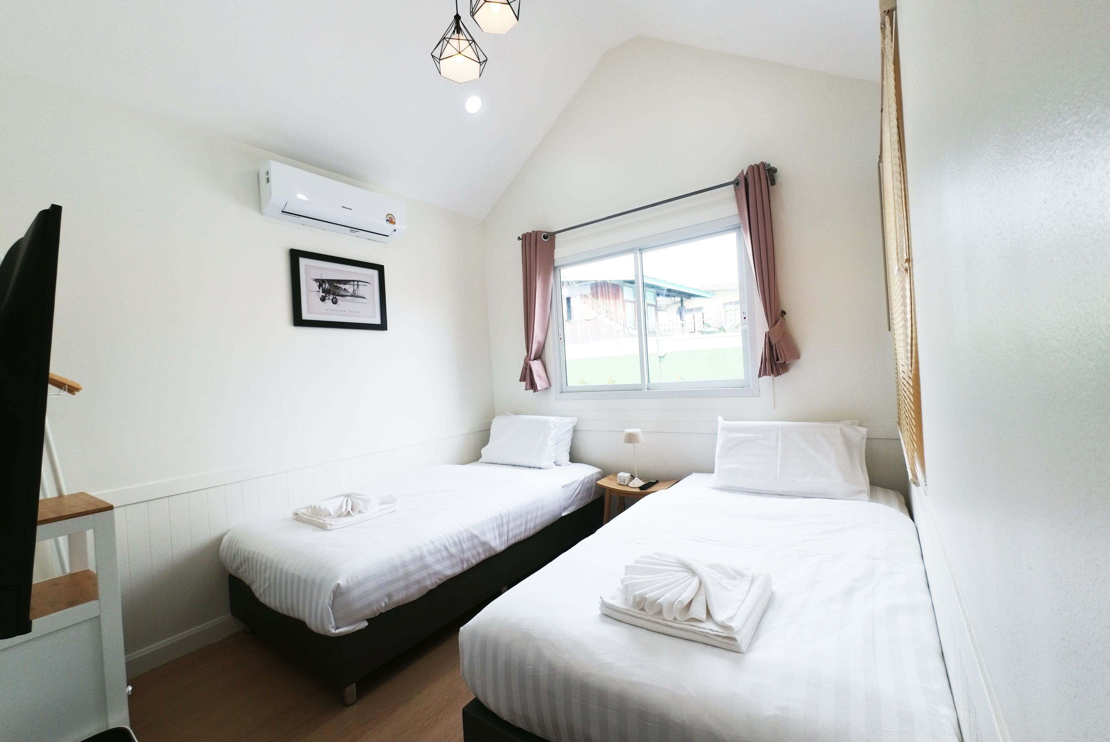 Habitación de hotel con dos camas, una ventana con cortinas, un cuadro en la pared y un equipo de aire acondicionado.