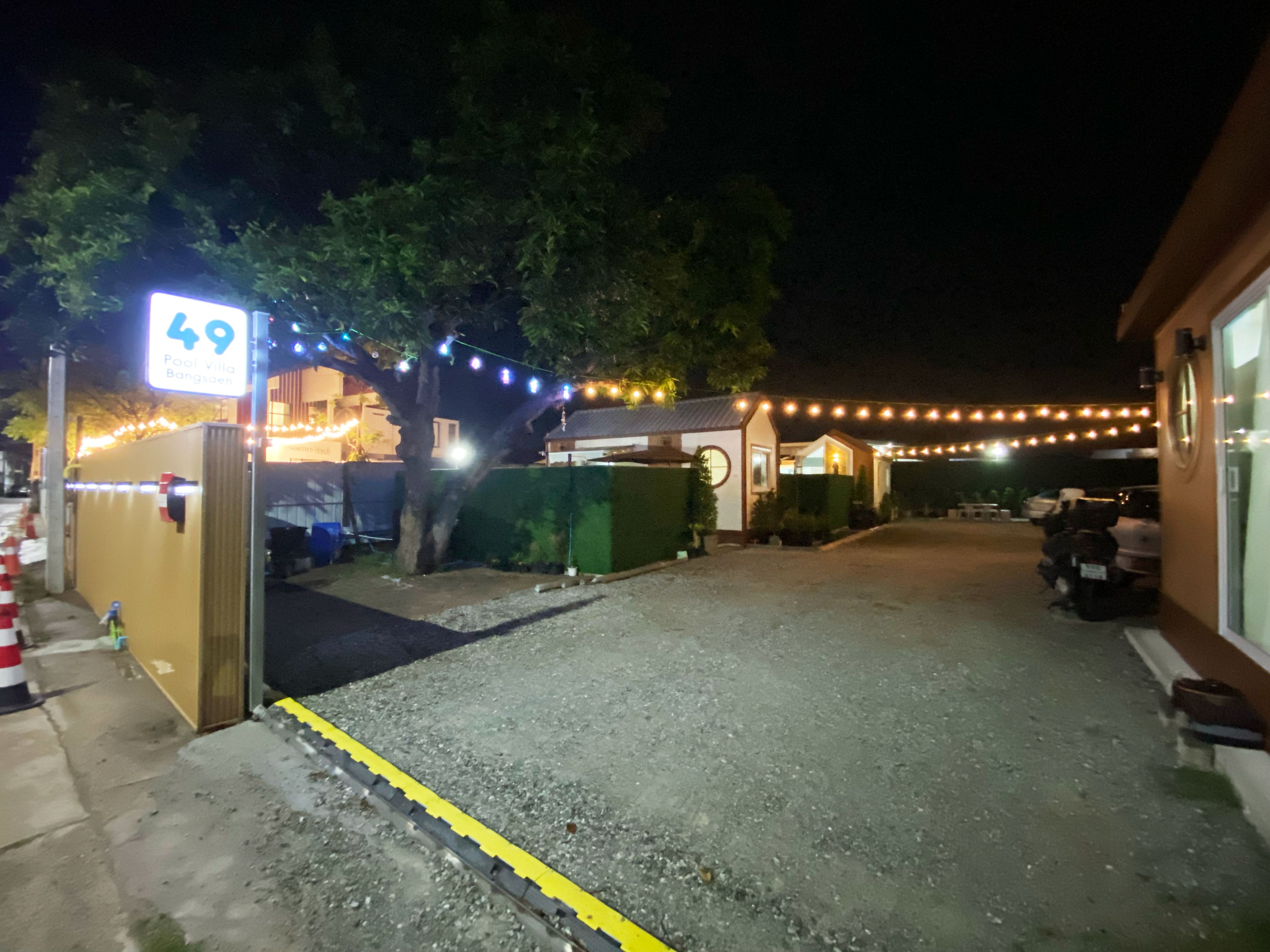 Vista nocturna de un edificio con un letrero que indica 'Pool Villa Bangsøen' y un área de estacionamiento con motocicletas.