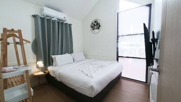 A hotel room with a bed, a bedside table, a hanging coat rack, a wall-mounted air conditioner, and a view of the city through the window.
