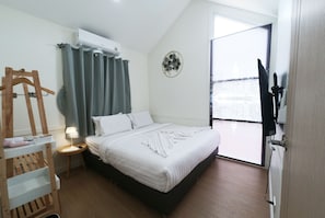 A hotel room with a bed, a bedside table, a hanging coat rack, a wall-mounted air conditioner, and a view of the city through the window. - 49 Pool Villa Bangsaen (Mueang Chonburi)